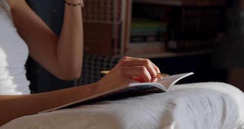 A Woman Drinking from a Cup While Writing on a Notebook