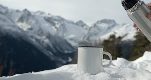 A Person Pouring Coffee into a Mug in the Snow