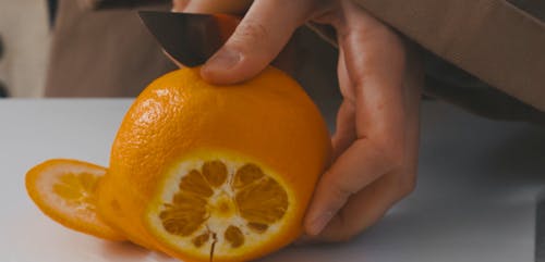 Person Peeling an Orange with Knife