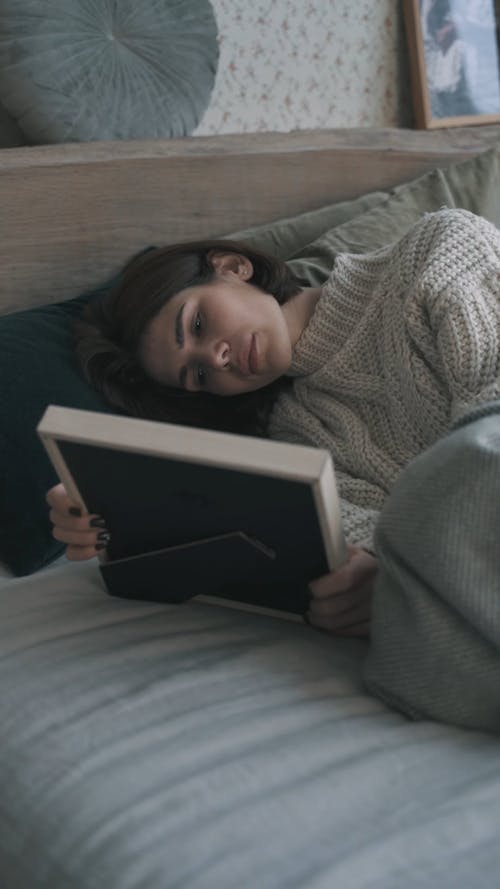 Emotional Woman Looking at Framed Photo while Lying on Bed