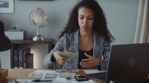 Female Accountant Counting Money While Using Her Laptop
