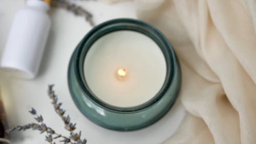 Lighted Candle With Lavender Flowers and Serum Bottles on a Surface