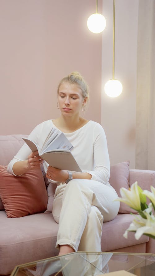 A Woman Flipping Pages of a Book While Sitting on a Couch