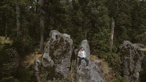 Drone Shot of a Man Sitting on a Rock Cliff in the Forest