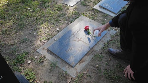 Man Placing Ball Of Baseball Over A Grave