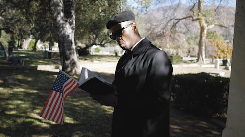 A Man Reading a Bible with a Flag in it in Front of a Grave