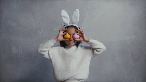 A Girl Wearing a Bunny Ears Headband While Covering Her Eyes with Easter Eggs