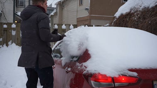 A Man Brushing Off Snow on Top of His Car