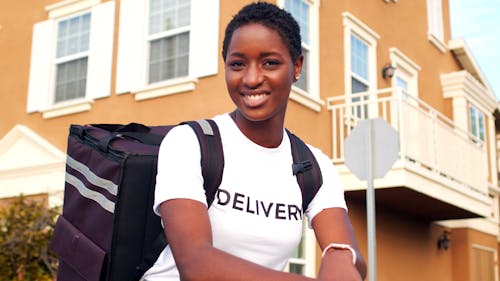 Delivery Woman with a Courier Backpack Standing on an Electric Scooter