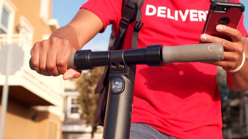 Close-Up View of Man Using a Cellphone while Riding an Electric Scooter