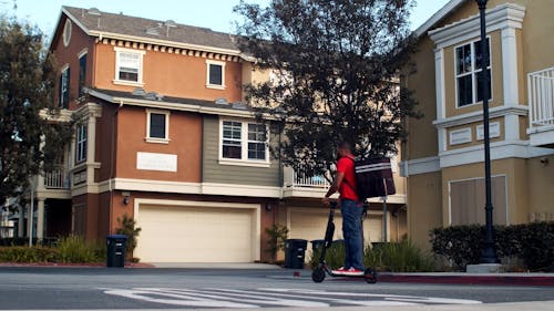 Man Carrying a Delivery Bag while Riding an Electric Scooter