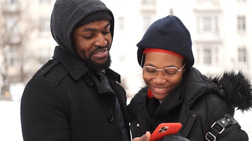 Man and Woman Looking at Cellphone Outside in the Snow