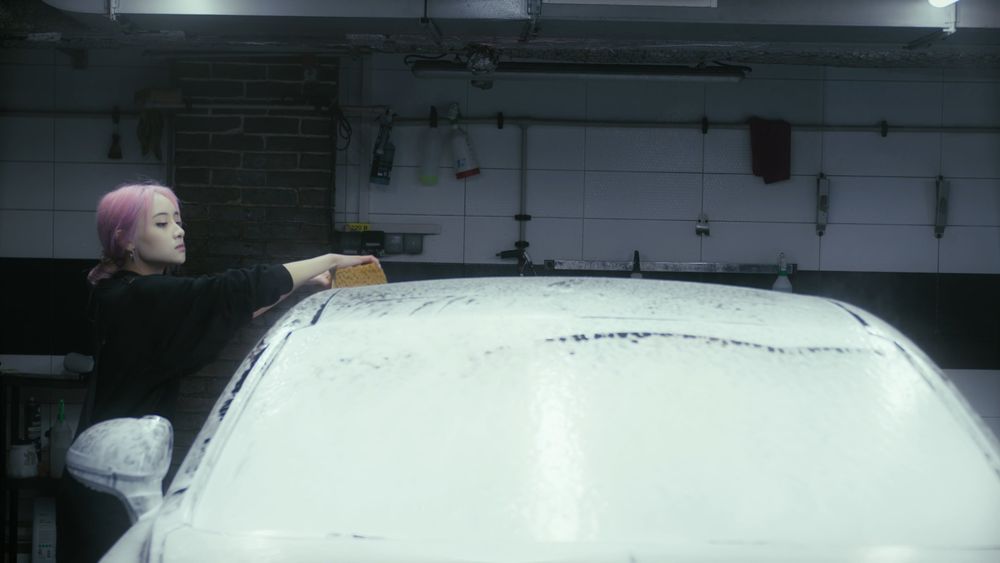 Asian woman washing a car exterior with a sponge