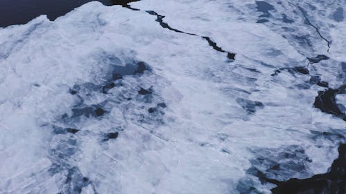 A Footage of an Ocean with Snow and a Snow Covered Cliff