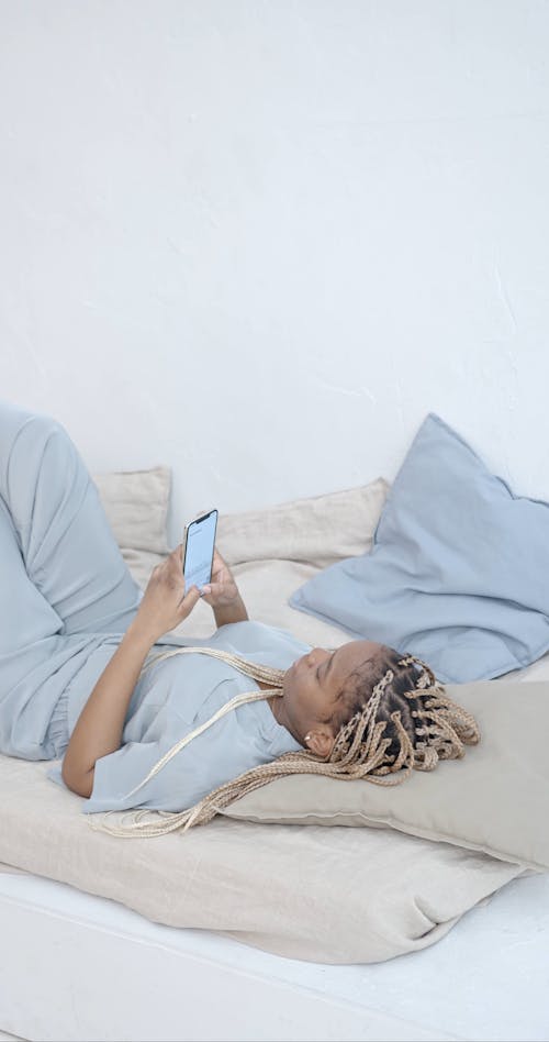 A Woman Typing on Her Cellphone While Lying on Her Bed