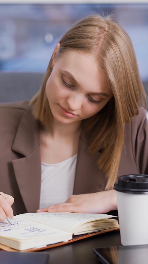A Woman Writing Notes while Drinking Coffee