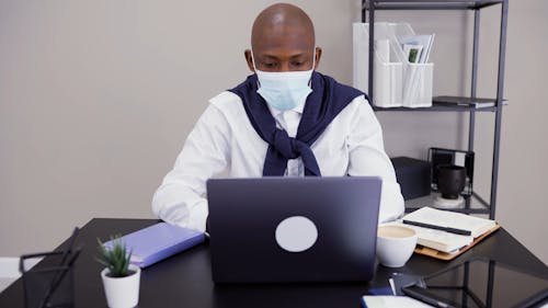 Man Typing on his Laptop while Writing Notes