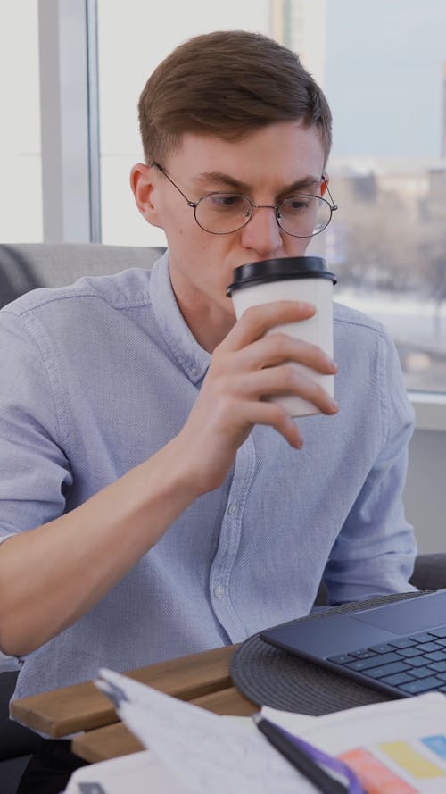 A Man Drinking Coffee while Using His Laptop