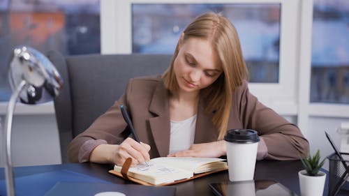 A Woman Writing while Holding a Cup of Coffee