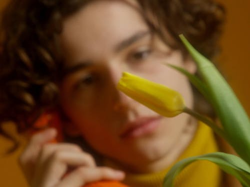 A Young Man Smelling A Flower While On A Phone Call