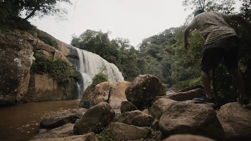 Man Sitting On Top Of Rock While Observes Waterfall