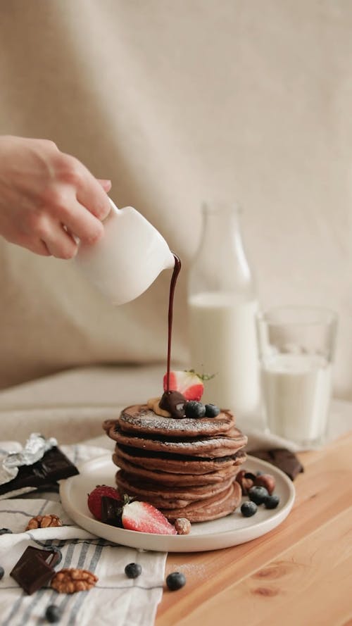 A Person Pouring Chocolate Syrup on Pancakes