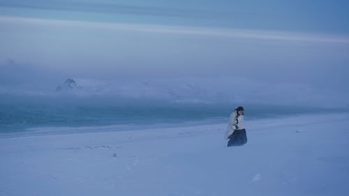 A Woman in Winter Clothing Walking on the Snow
