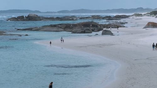 People Walking on a White Sand at the Rocky Shore