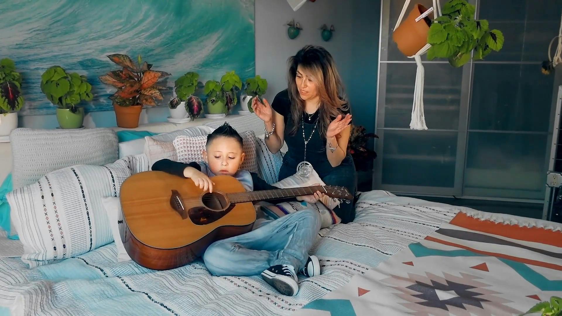 Boy Trying To Play A Guitar While Her Mother is Cheering · Free Stock Video