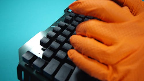 Person Wearing Orange Gloves Typing on a Keyboard