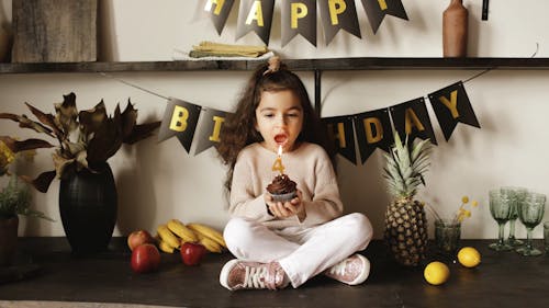 Girl Blowing the Lighted Candle on a Birthday Cupcake
