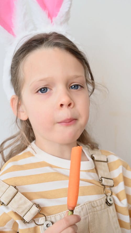 Little Girl Wearing Bunny Ears while Eating a Carrot