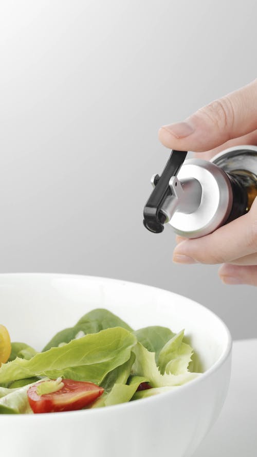 Person Pouring Oil on Salad