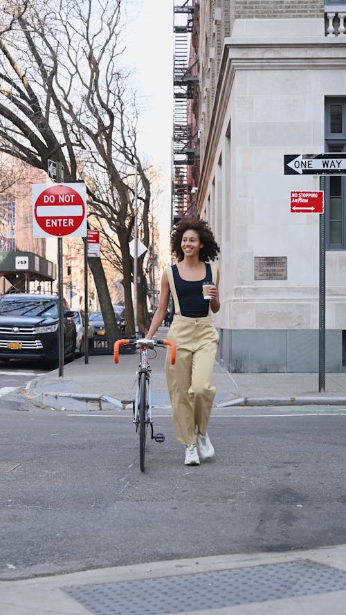 A Woman Crossing the Street While Holding a Coffee Cup and a Bike