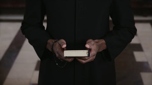 A Priest Holding a Bible and a Rosary