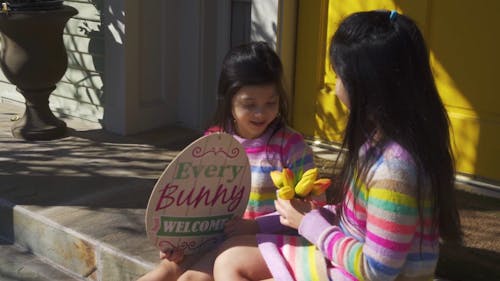 Sisters Sitting Outdoor while Holding Easter Decorations