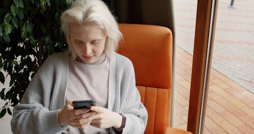 Woman Sitting on a Chair While Using Cellphone