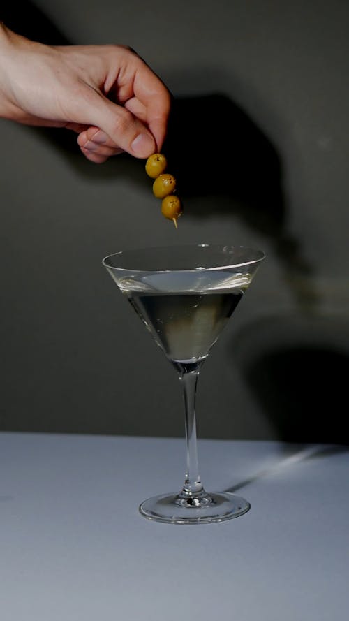 Person Putting Green Olives on a Alcoholic Beverage