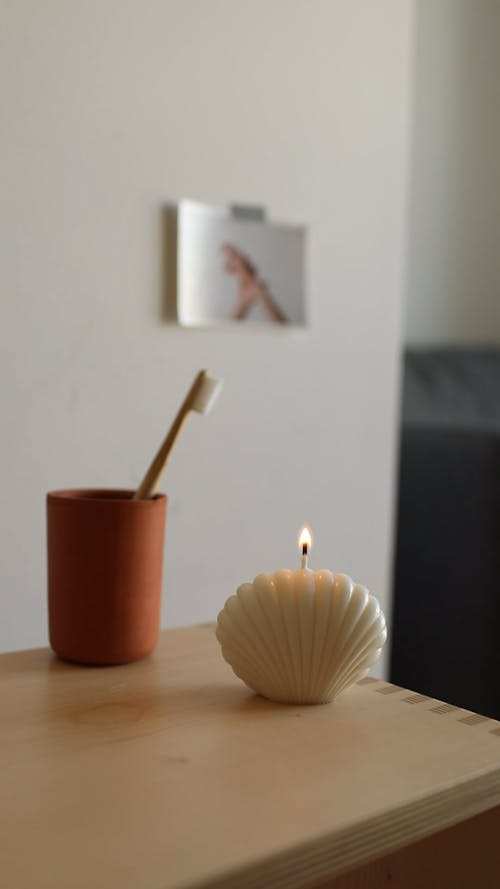 A Seashell Shaped Candle Beside a Cup with a Toothbrush Above the Table