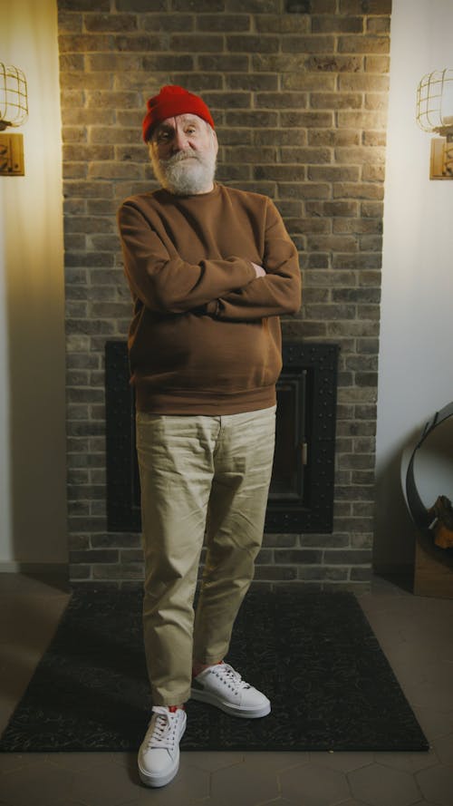 Man Wearing Brown Sweater Standing In Front of a Fireplace