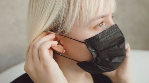 A Woman Putting Face Mask Strap on Her Ear