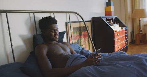 Man Lying on Bed While Using Cellphone