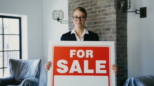 A Real Estate Agent Holding CArdboard Stating For Sale