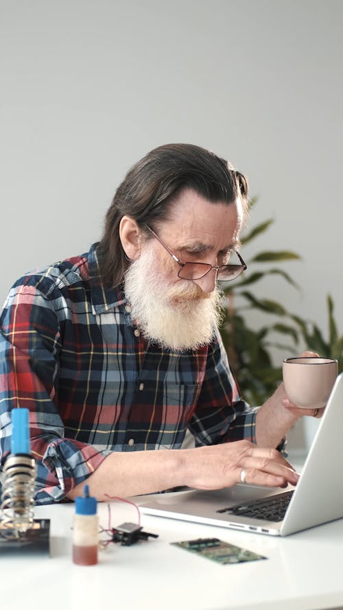 An Elderly Man Drinking Coffee while Using a Laptop