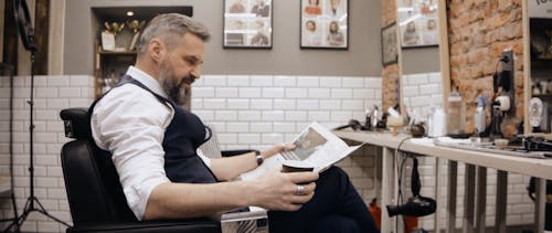 Businessman Reading a Newspaper and Drinking Coffee at the Barbershop