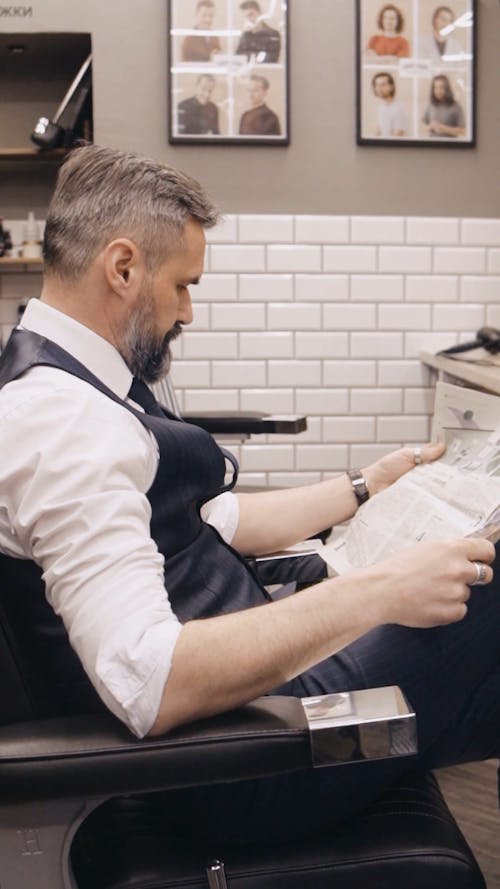 A Man Sitting while Reading a Newspaper in the Barbershop