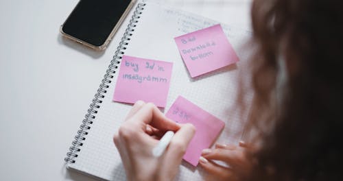 Person Writing on Pink Sticky Notes