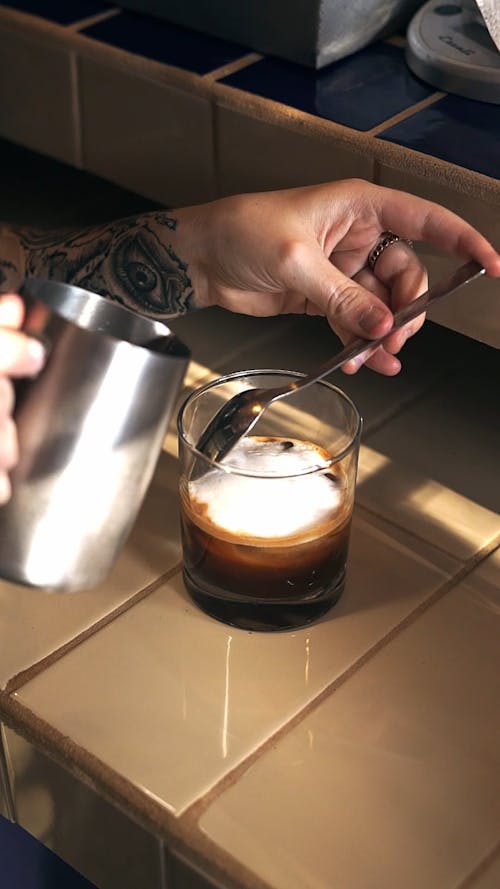 A Person Pouring Milk in a Glass with Coffee