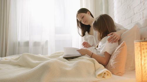 A Woman Reading a Book with her Daughter in Bed