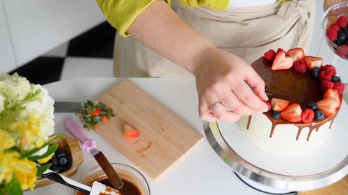 Person Decorating the Cake while Putting Strawberry, Blueberry and Rasberry Fruits